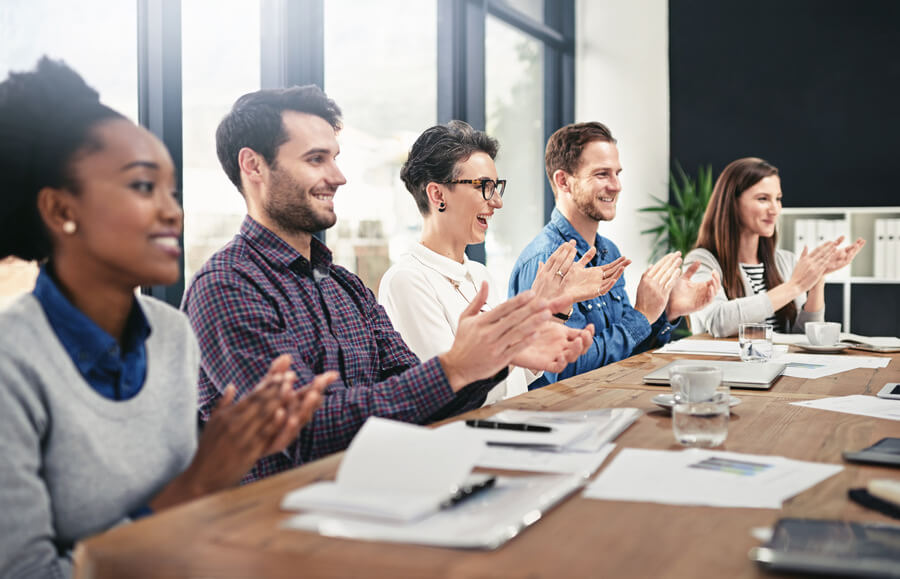 Equipo de trabajo en reunión aplaudiendo y sonriendo en oficina moderna.
