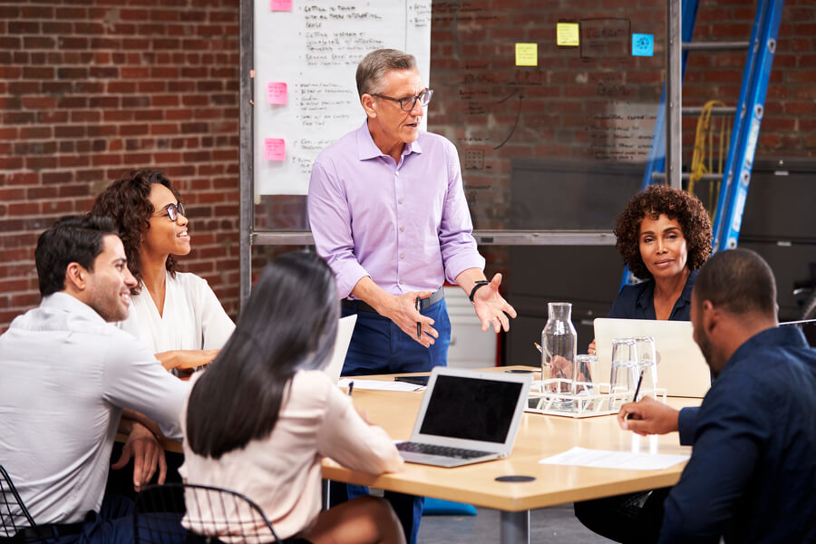 Estrategias para atraer talento humano importancia - Líder de equipo explicando ideas durante una reunión de trabajo con colegas en una oficina moderna con pared de ladrillo.
