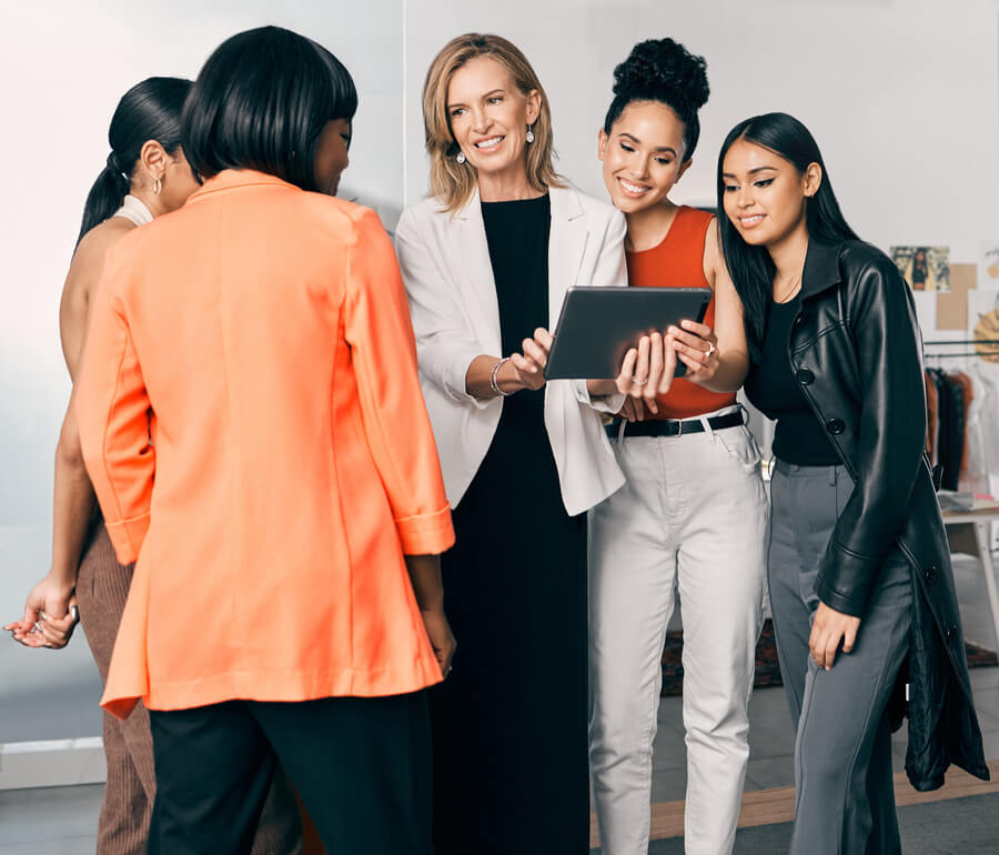 Proceso de reclutamiento y selección fases - Grupo de mujeres observando una tablet y sonriendo en un entorno de oficina o showroom creativo.