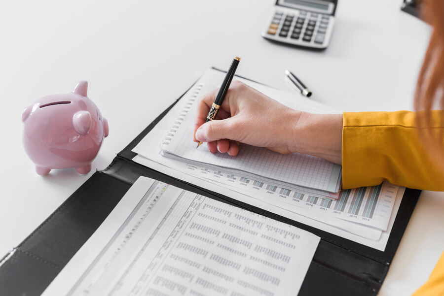 Sistemas de pagos de nómina en Colombia - Persona revisando y anotando finanzas con calculadora y alcancía.