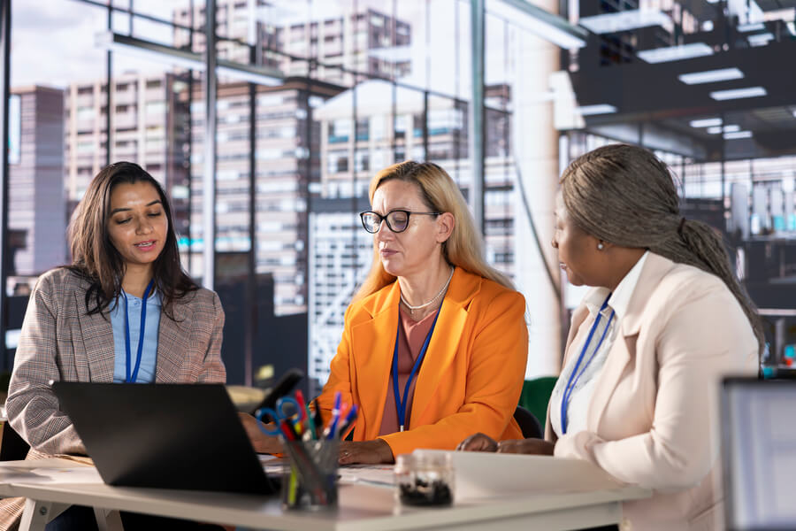 Payrolling que es como funciona - Tres mujeres ejecutivas en reunión frente a una laptop en oficina corporativa.