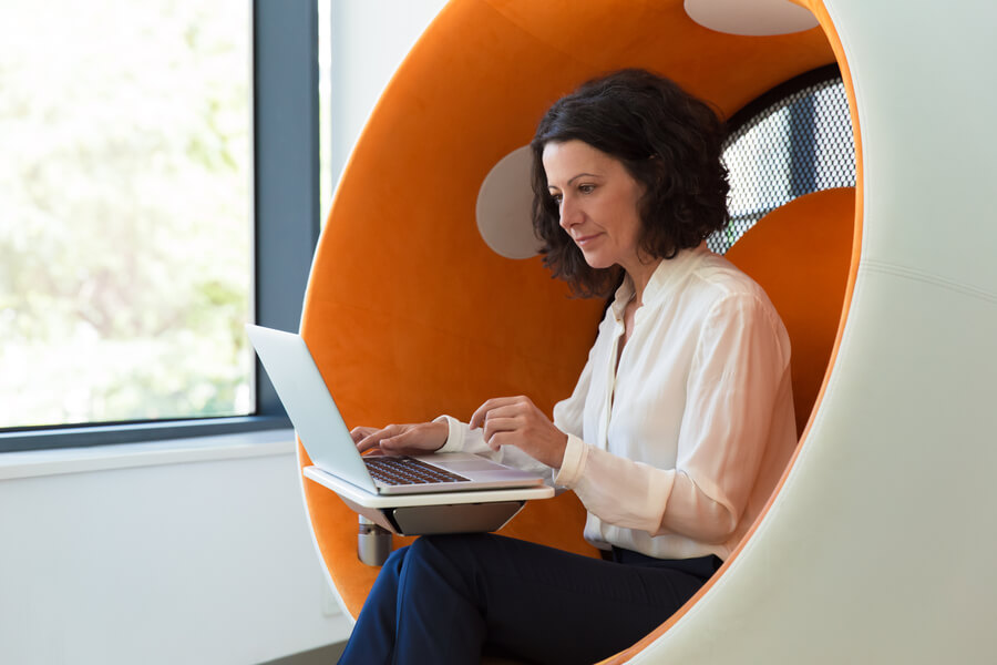Técnicas de selección de personal características - Mujer trabajando en laptop dentro de una silla cápsula moderna.