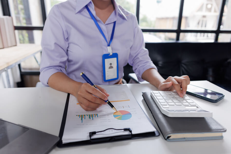 Persona trabajando con gráficos financieros y usando una calculadora en la oficina.
