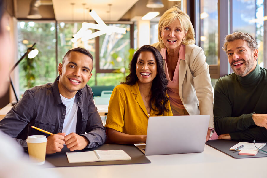 Evaluar el desempeño de los empleados - Grupo de personas sonriendo en reunión de trabajo con portátil.