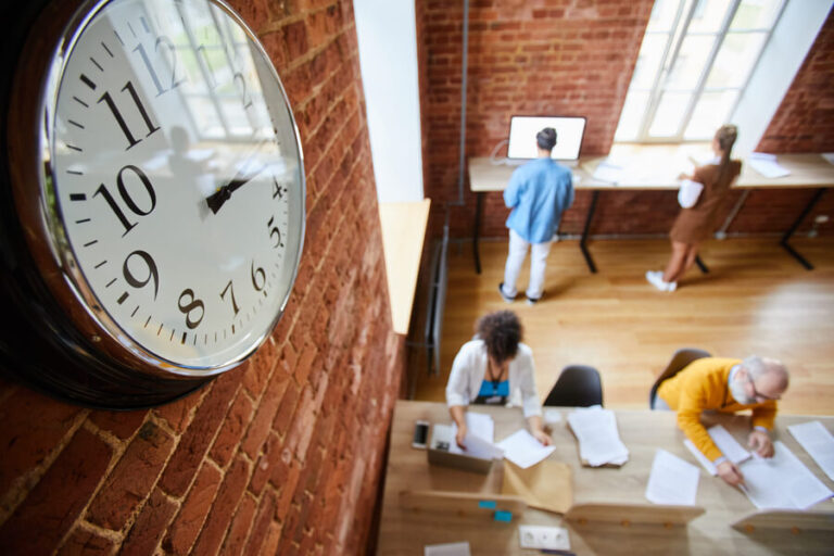 Reloj de pared grande en una oficina con personas trabajando