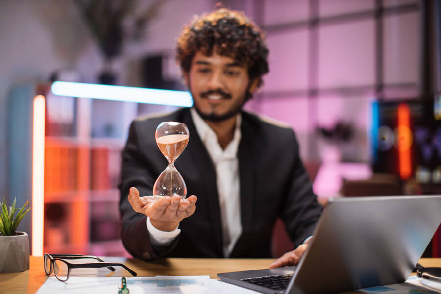 Hombre sosteniendo un reloj de arena frente a una computadora portátil